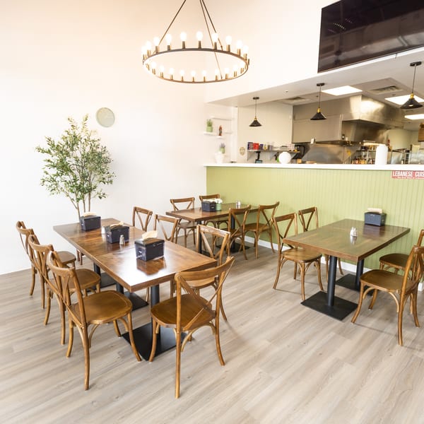 Bright, modern Lebanese restaurant interior with wooden tables, chairs, and a light green counter.