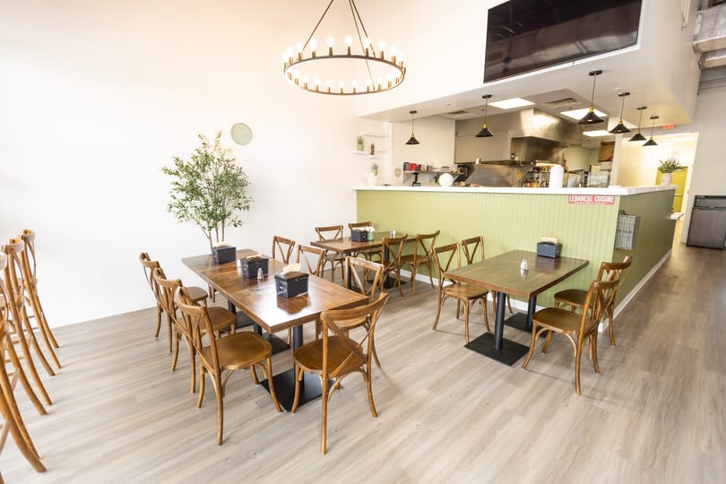 Bright, modern Lebanese restaurant interior with wooden tables, chairs, and a light green counter.