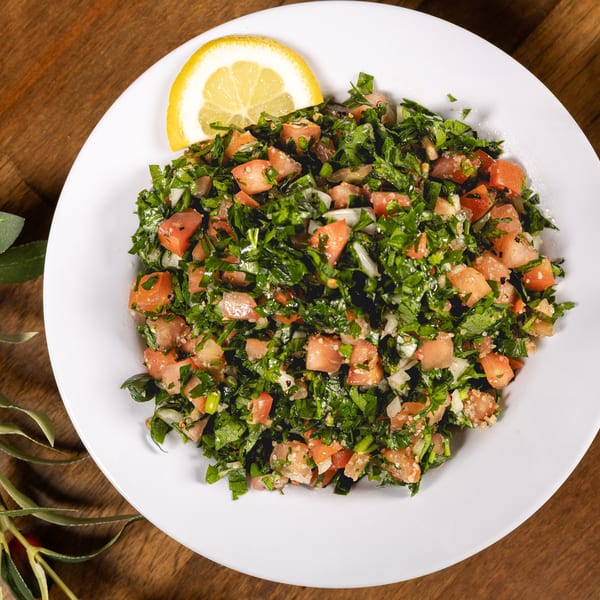 Tabbouleh salad with chopped parsley, tomatoes, and a lemon slice on a white plate.