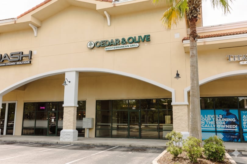 Exterior of Cedar & Olive Mediterranean Grill storefront with a palm tree and arched walkways.