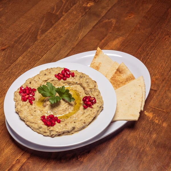 Baba Ghanoush with pomegranate seeds, parsley, and olive oil, served with pita bread on a wooden table.