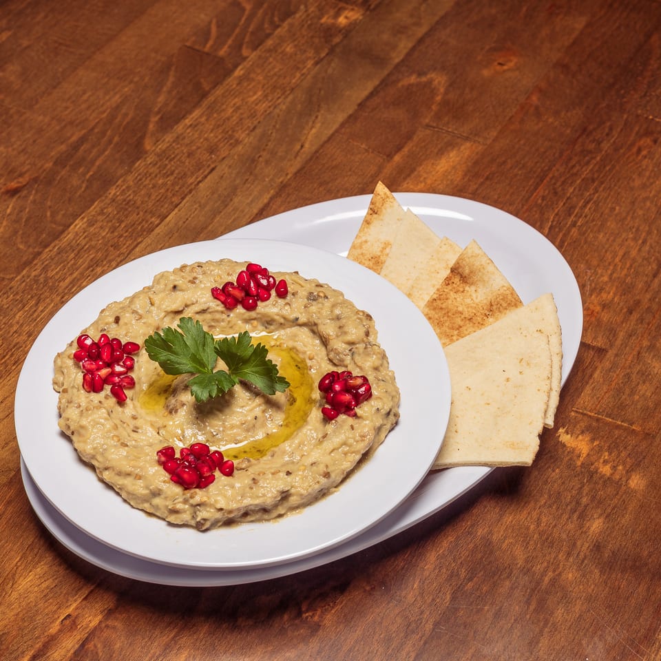 Baba Ghanoush with pomegranate seeds, parsley, and olive oil, served with pita bread on a wooden table.