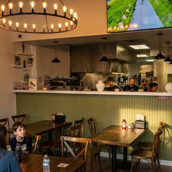 Diners seated at tables in a casual restaurant with an open kitchen and staff behind the counter.